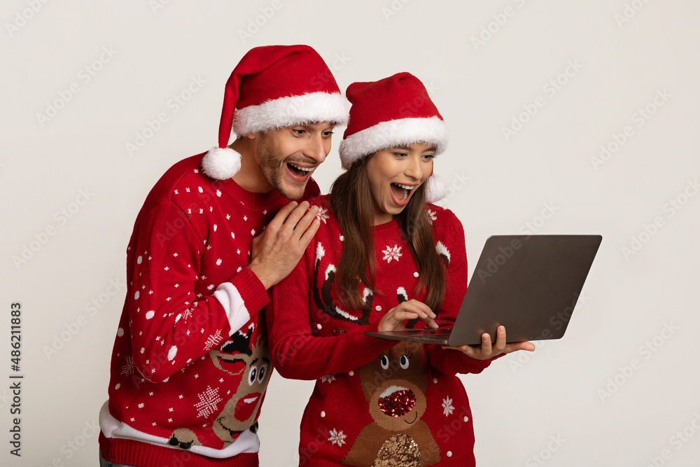 Online Win. Happy Excited Couple In Santa Hats Looking At Laptop Screen Online Win. Happy Excited Couple In Santa Hats Looking At Laptop Screen