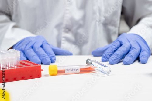 Medical covid test tube with contaminated blood and sealed vaccine bottle with doctor on the background