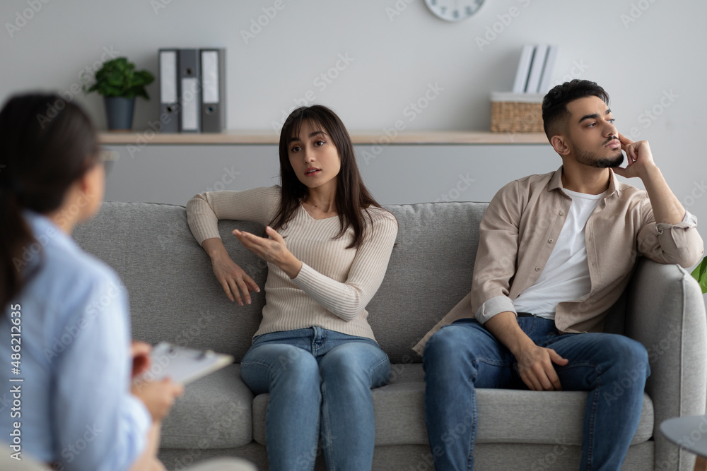 Unhappy arab woman talking about problems and breakup with professional marriage consultant, husband listening Unhappy arab woman talking about problems and breakup with professional marriage consultant, husband listening