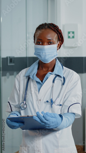 Portrait of woman working as doctor with white coat and stethoscope, standing in hospital ward. Medical specialist wearing face mask being ready to treat ill patient with medicine