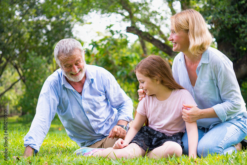 happy family elderly caucasian and child caucasian sitting on lawn relax in weekend holiday lifestyle in park . © HappyTime 17