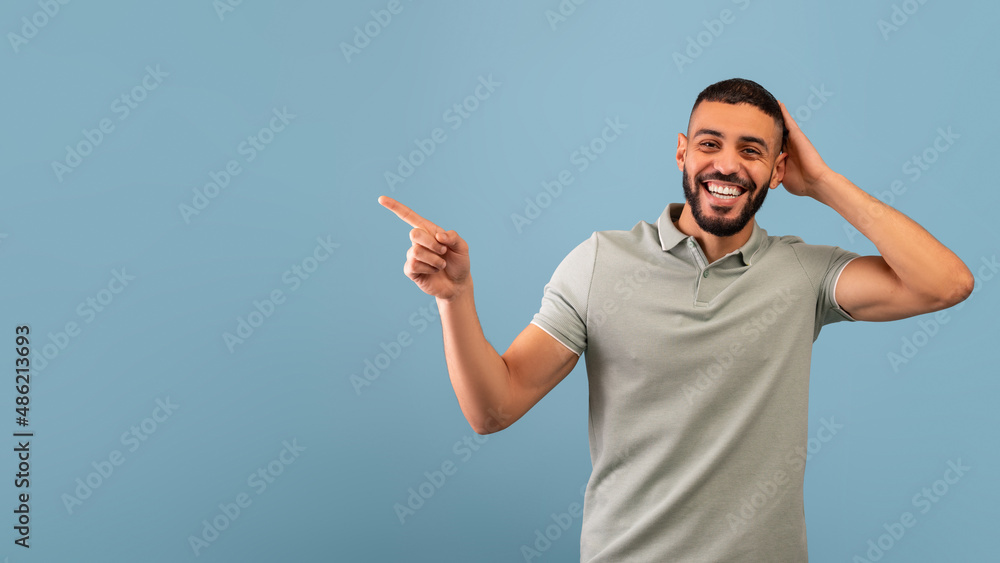 Fototapeta premium Look at this offer. Excited arab man pointing aside showing empty space for your text or ad, blue background