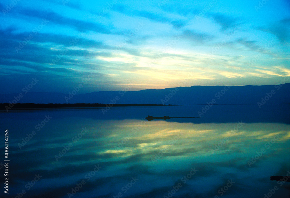 Mountains and clouds reflected in perfect symmetry in the Dead Sea in the early morning blue light at sunrise.