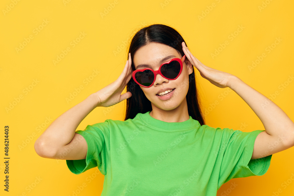 Portrait Asian beautiful young woman in dark glasses in a green t-shirt posing modern yellow background unaltered Portrait Asian beautiful young woman in dark glasses in a green t-shirt posing modern yellow background unaltered