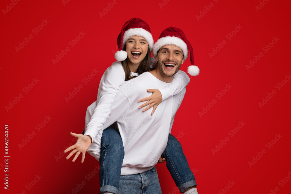Xmas Mood. Cheerful Couple Wearing Santa Hats Having Fun On Red Background Xmas Mood. Cheerful Couple Wearing Santa Hats Having Fun On Red Background