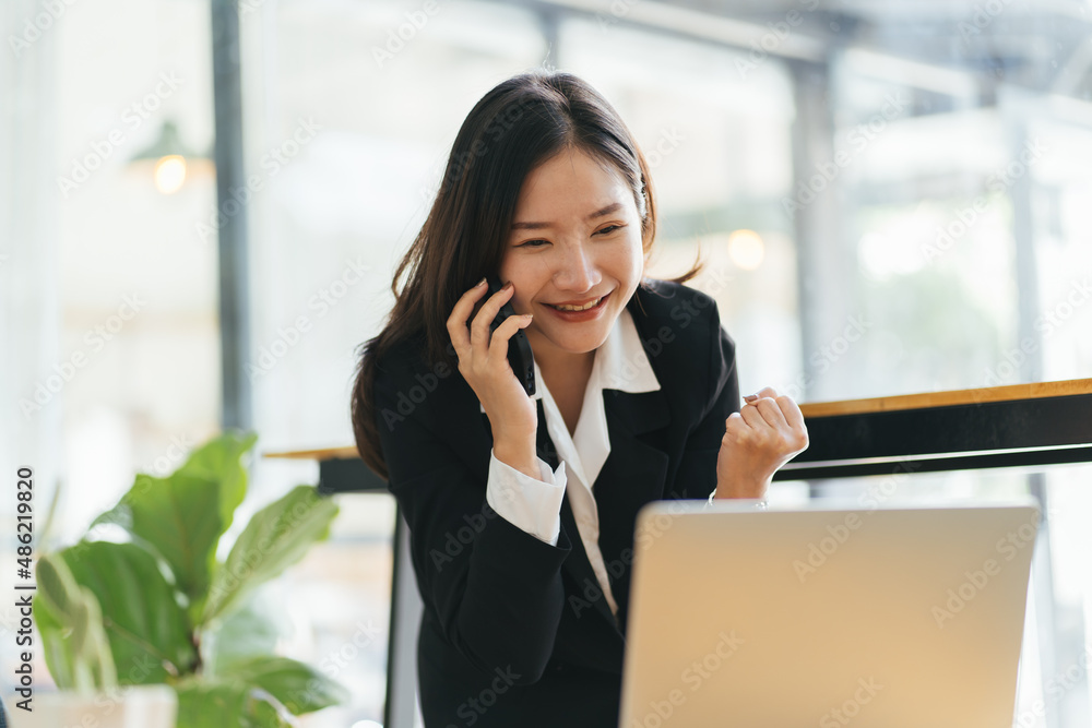 Happy young asian woman talking on the mobile phone and smiling while sitting at her working place in office. Happy young asian woman talking on the mobile phone and smiling while sitting at her working place in office.