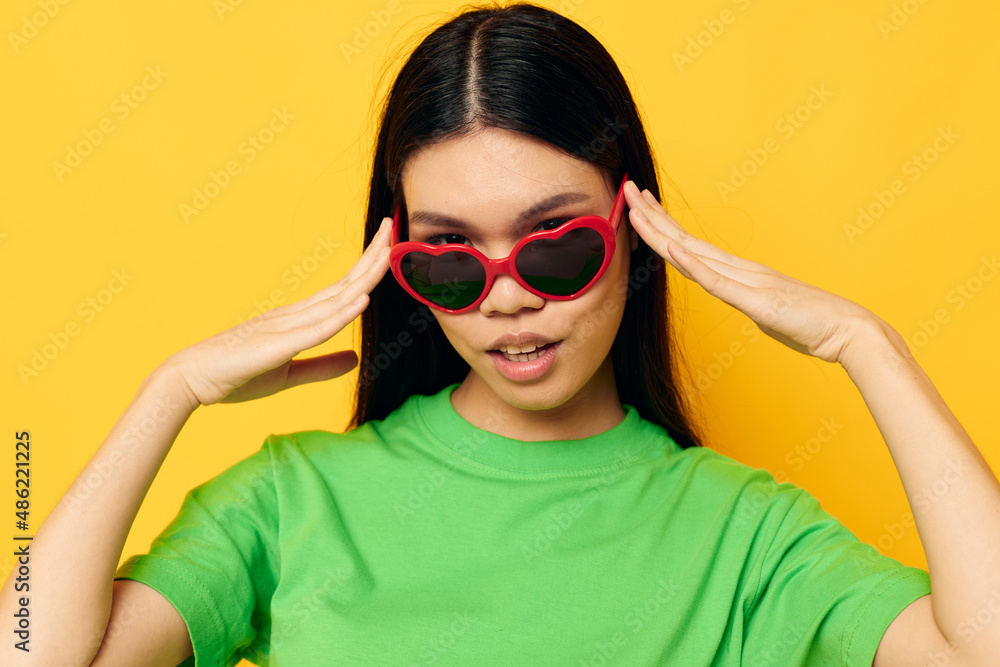 Portrait Asian beautiful young woman in dark glasses in a green t-shirt posing modern yellow background unaltered Portrait Asian beautiful young woman in dark glasses in a green t-shirt posing modern yellow background unaltered
