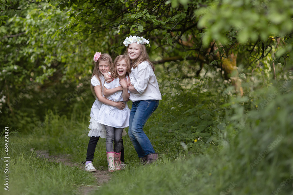 Three teenage girls in white blouses are laughing and playing, friendly hugging. Children's fun in nature in summer, holidays, happy childhood concept Three teenage girls in white blouses are laughing and playing, friendly hugging. Children's fun in nature in summer, holidays, happy childhood concept