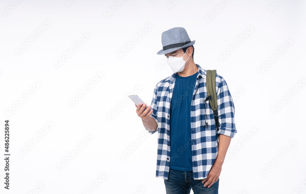 Traveler young man wear face mask with backpack protect outbreak flu ncov looking smartphone own hand standing over isolated white background. Lifestyle people travel new normal safety concept. Traveler young man wear face mask with backpack protect outbreak flu ncov looking smartphone own hand standing over isolated white background. Lifestyle people travel new normal safety concept.