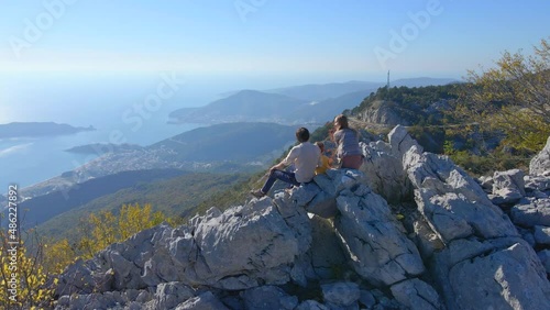 Aerial shot. Family of toursts father mother and son visit the Fortress Kosmach in Montenegro. Drone rotates around them as they stand on a hill observing the city of Budva in the distance photo