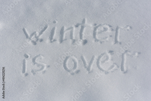 Inscription Winter is over, written on white surface of the snow. Top view. Flat lay. Winter holiday concept. Sunlight.