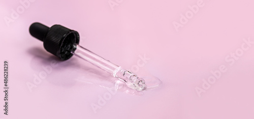 Pipette with fluid hyaluronic acid on pink background. Cosmetics and healthcare concept closeup. Dose of serum, retinol with air bubbles. Flat lay. Luxury beauty product presentation, macro. Banner