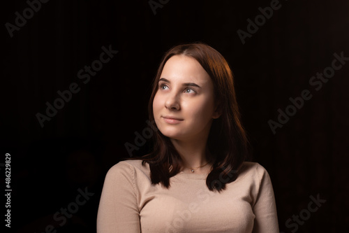 Young woman pensive. Looking away. Dark background. Girl with brown hair in a sweater. Reflections, thoughts.