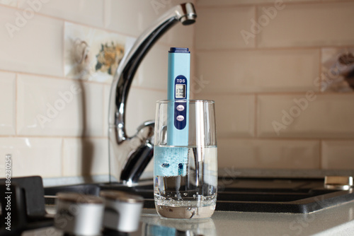 TDS measurement of water. Electronic pH meter in a glass of water. In the background there is a tap for drinking water. The concept of testing water for miralization