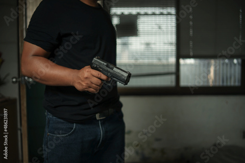 Man holding a pistol, standing in a room in black, pointing and aiming a gun at a target. concept of assassination, murder, criminal