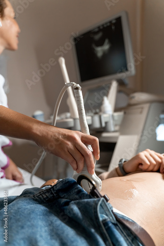 Ultrasound diagnostics of the stomach on the abdominal cavity of a girl in the clinic, close-up. The doctor holds the ultrasound probe over the patient's abdomen. Internal organs diagnostics.