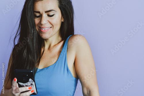 Cheerful smiling woman in looking at the phone  reading a Message  checking social media  shopping online   ordering delivery  against pink wall  connected to high speed internet