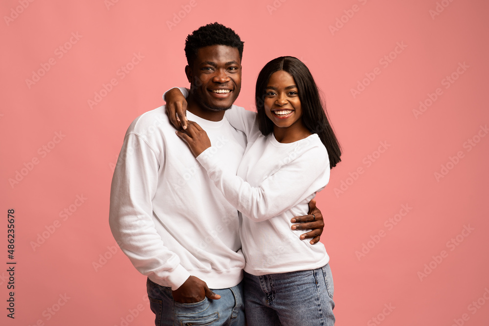 Fototapeta premium Cheerful young black lovers embracing on pink