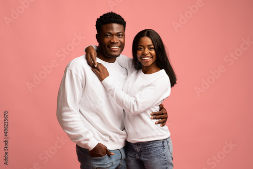 Cheerful young black lovers embracing on pink
