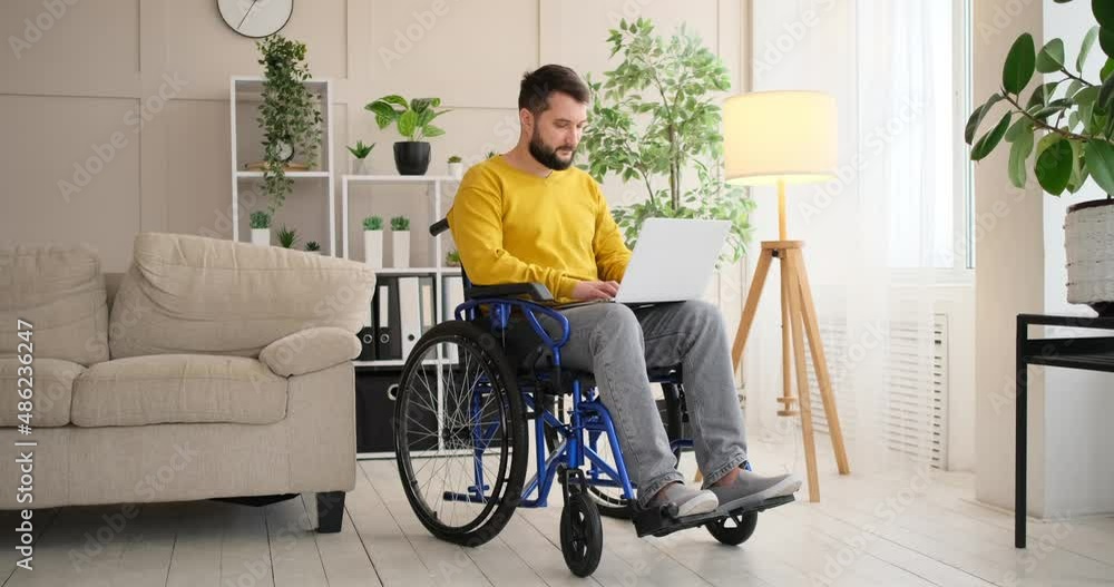Disabled man on wheelchair working with laptop at home Disabled man on wheelchair working with laptop at home