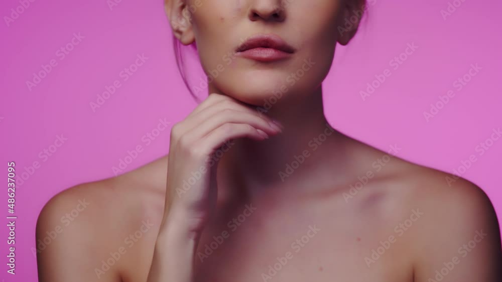 Woman runs finger along chin after using cosmetic cream while standing on pink background in studio, front view. Woman uses skin care products Woman runs finger along chin after using cosmetic cream while standing on pink background in studio, front view. Woman uses skin care products