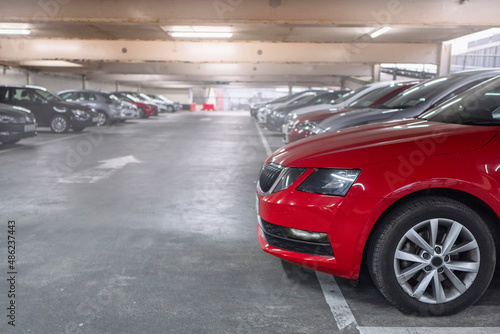 Row of cars in a car park or dealership. Selective focus. Red color car in foreground. Busy parking lot of a shopping mall. Parking prices and vehicle density in town issue. Soft cinematic look © mark_gusev