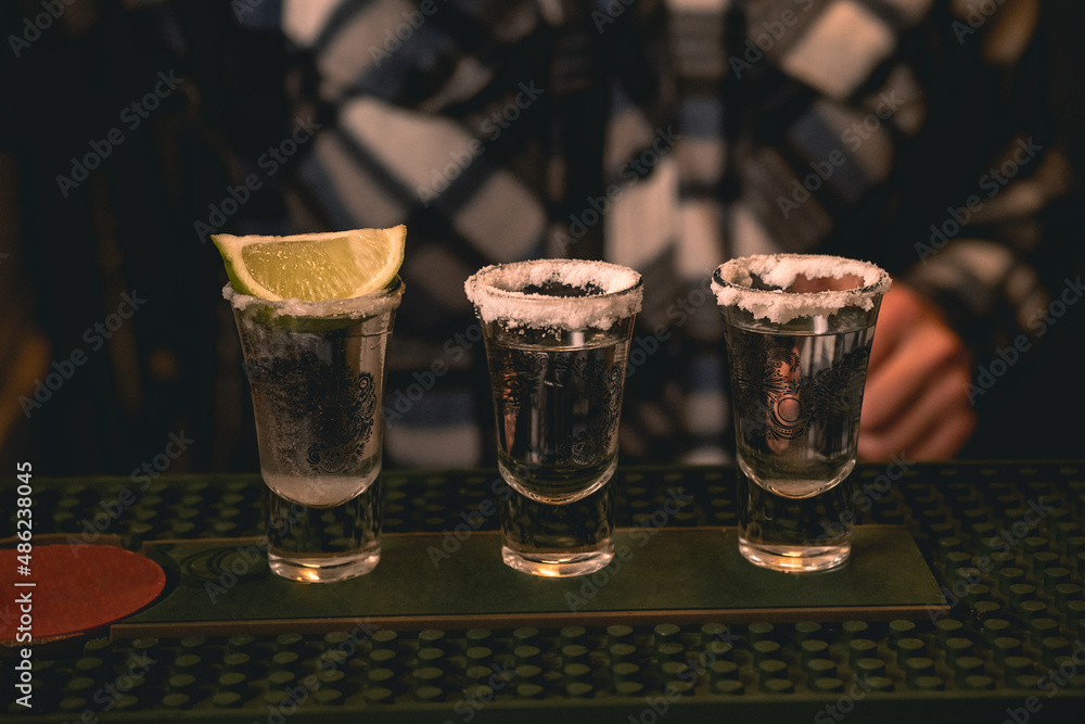 Three tequila shot rimmed with salt served with lime on bar counter