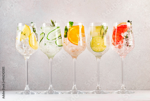 Gin and tonic cocktails set. Trendy Alcoholic drinks with lime, lemon, grapefruit, orange, cucumber, soda and spicy herbs in wine glasses, gray background. Summer cocktail party