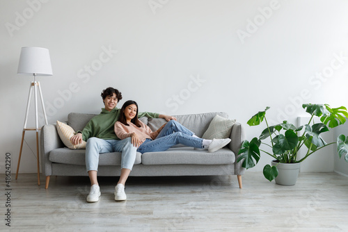Affectionate young Asian couple cuddling on couch in living room, spending time together, free space