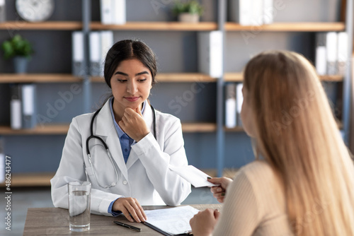 Serious millennial indian woman therapist in uniform, think, looks at envelope with money from client