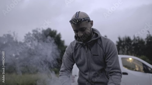 A young bald man preparing bee smoker. The apiary worker wearing a head torch and lighting up a bee smoker. photo