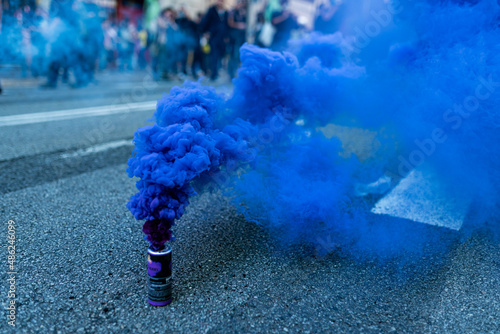 A blue smoke bomb is seen among protesters marching during a protest in the street with people uprising photo