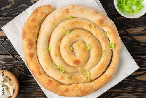 Banitsa - traditional Bulgarian spiral shape pie with brynza cheese and green onion are on brown wooden background photo