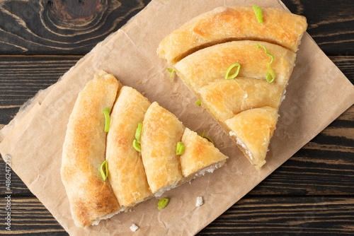Banitsa - traditional Bulgarian spiral shape pie with brynza cheese and green onion are on brown wooden background. photo