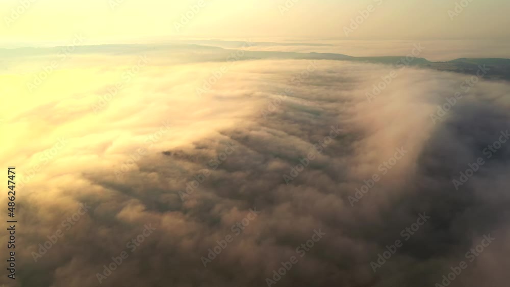 A thick fog illuminated by the sun envelops the fields at dawn. Filmed 4k, drone video.