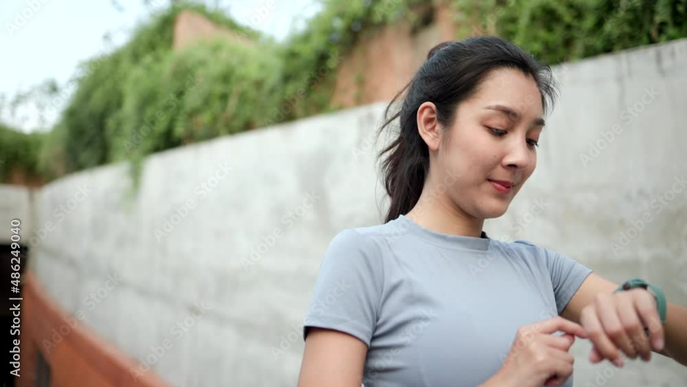 Slim beautiful woman checking sports smart watch in the city at sunrise. Asian female adjusting smart watch before workout outdoor. Exercise in the morning. Healthy and active lifestyle concept. Slim beautiful woman checking sports smart watch in the city at sunrise. Asian female adjusting smart watch before workout outdoor. Exercise in the morning. Healthy and active lifestyle concept.