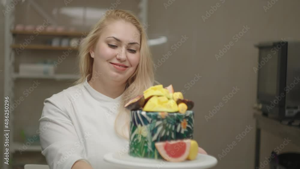 Young adult woman chef decorating cake with mango, passion fruit, grapefruit and blueberry. Confectionery bakery process in slow motion. Young adult woman chef decorating cake with mango, passion fruit, grapefruit and blueberry. Confectionery bakery process in slow motion.