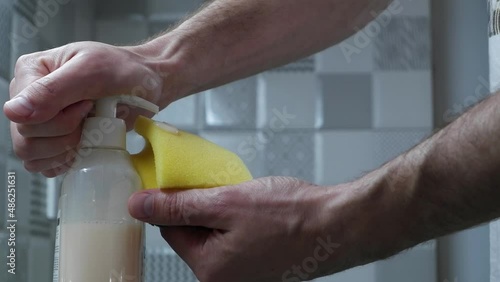 a close-up shows how a hand pours liquid dishwashing detergent onto a yellow sponge and a man's hand squeezes this sponge