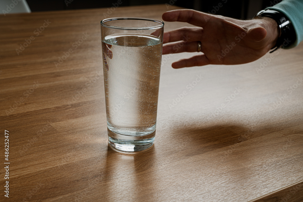 Man's hand stretches to a glass of water Man's hand stretches to a glass of water