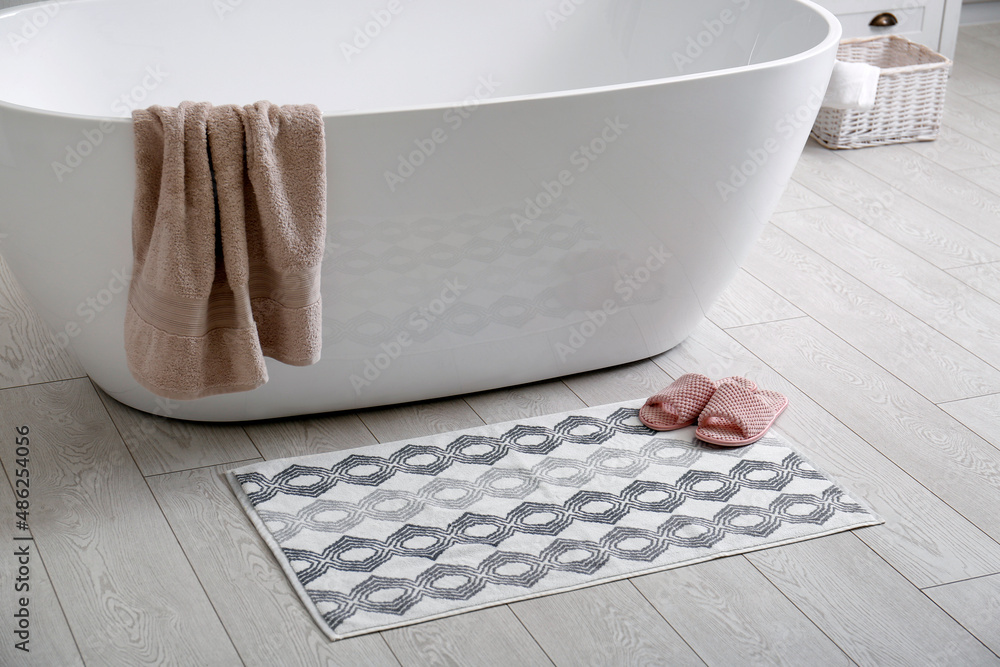 Stylish mat and slippers on floor near tub in bathroom. Interior design - obrazy, fototapety, plakaty 