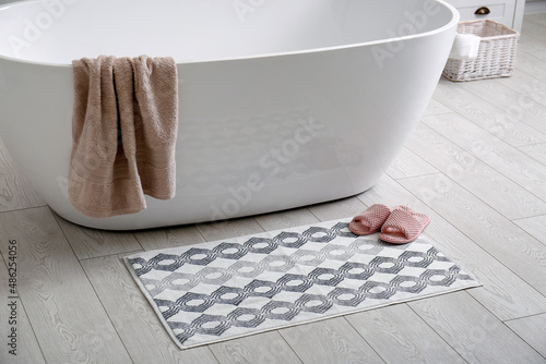 Stylish mat and slippers on floor near tub in bathroom. Interior design
