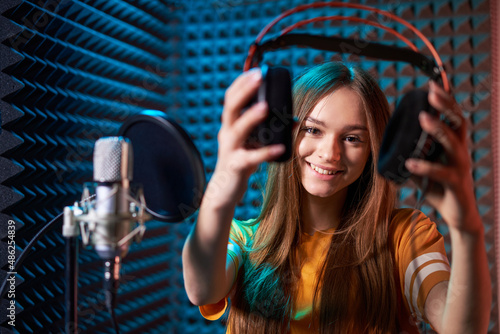 Girl in recording studio in headphones with mic over absorber panel background with closed eyes photo