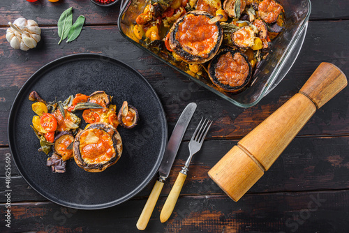 Served portobello  mushrooms,baked and stuffed with cheddar cheese, cherry tomatoes and sage on black plate over  old wooden table  top view photo