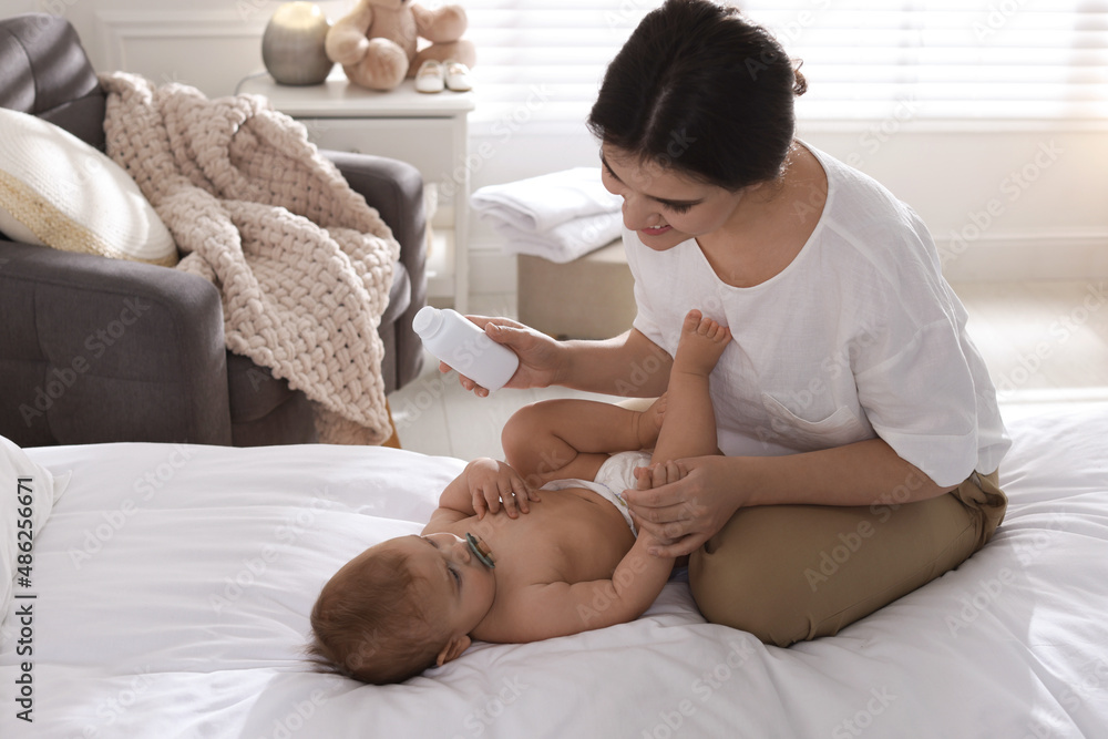 Mother with bottle of dusting powder and her cute baby at home, space for text Mother with bottle of dusting powder and her cute baby at home, space for text
