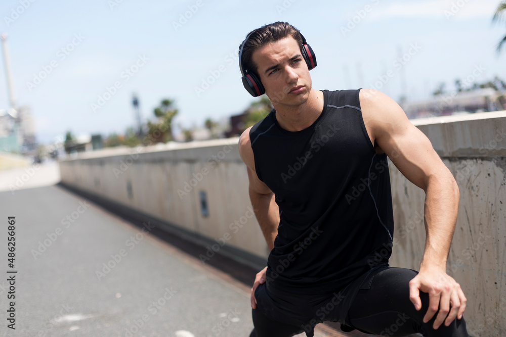 Sporty man with headphones stretching his legs outdoors.