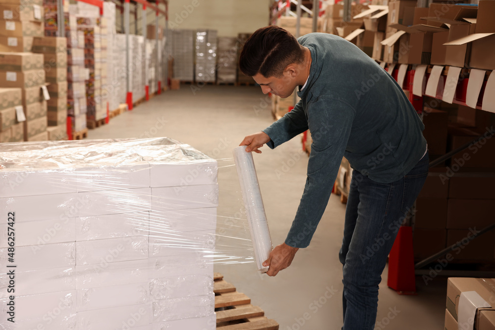 Worker wrapping boxes in stretch film at warehouse Worker wrapping boxes in stretch film at warehouse