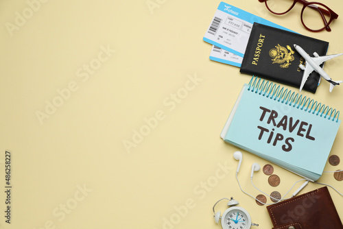 Notebook with phrase Travel Tips and tourist items on yellow background, flat lay. Space for text