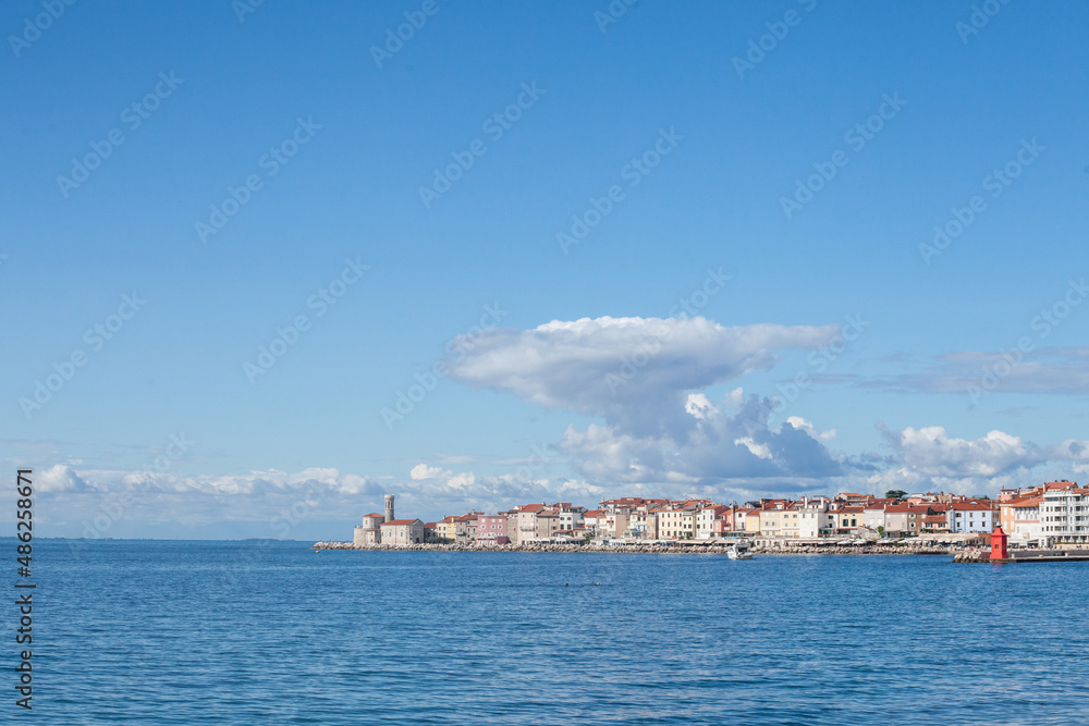 Panorama of  Piran, Slovenia, with the Adriatic sea in front, with blue water and sky, on a wharf and quay, during a summer afternoon. Piran, or Pirano, is slovenian city on adriatic sea in istria