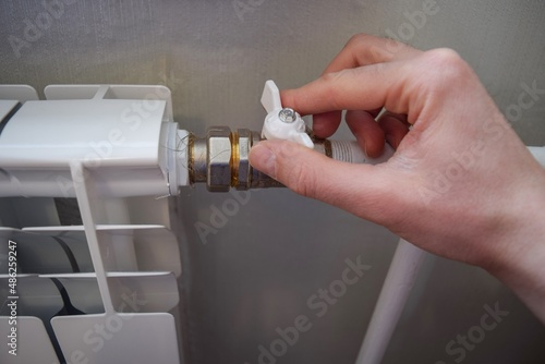 A man's hand turns the valve of a home heating radiator