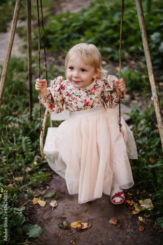 Happy baby girl on a swing in the summer in the park. A little girl in a dress with a full skirt in the park.